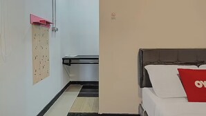 Una habitación de hotel con una cama, un almohadón rojo, un panel de madera en la pared y un cesto de basura.