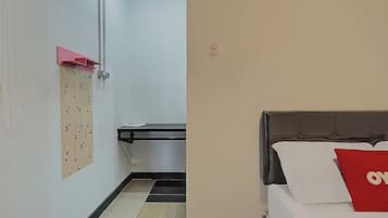 A hotel room with a bed, a red pillow, a wooden panel on the wall, and a trash bin.