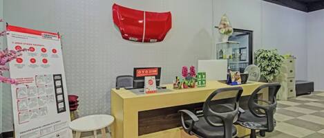 A reception desk with a computer, a telephone, and a small plant. There is a poster on the wall and a chair in front of the desk.
