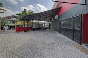 A paved courtyard with a covered area, a red gate, and a building with a red door. - Super OYO 3198 Sukomanunggal Inn (Surabaya)