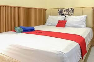 A neatly made bed with white bedding, a red throw, and a blue towel.