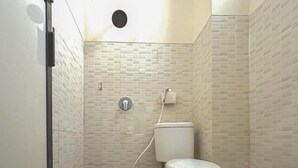 Et badeværelse med toilet, bruser og væghængt vask.