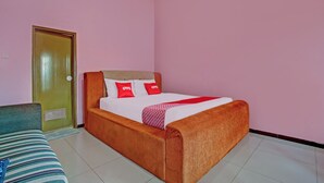 A single bed with a wooden headboard, a green door, and a pink wall. - OYO 3866 Villa Gothick (Batu)