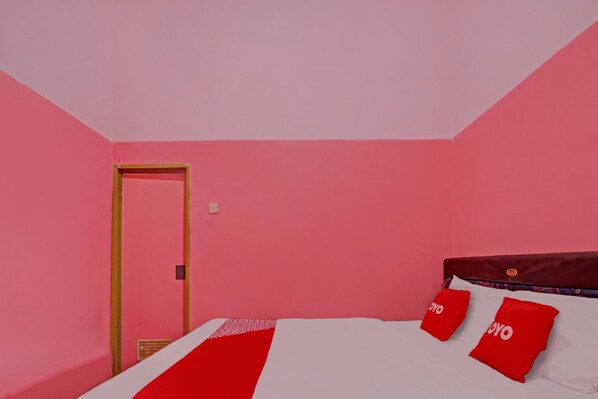 A room with pink walls, a wooden door, and a bed with red and white bedding and pillows. - OYO 3866 Villa Gothick (Batu)
