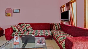 A living room with a red sofa, a glass coffee table, and a television on a stand. - OYO 3866 Villa Gothick (Batu)