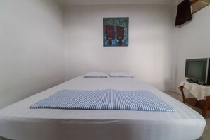 Une chambre avec un lit simple et une télévision posée sur une table, à droite.