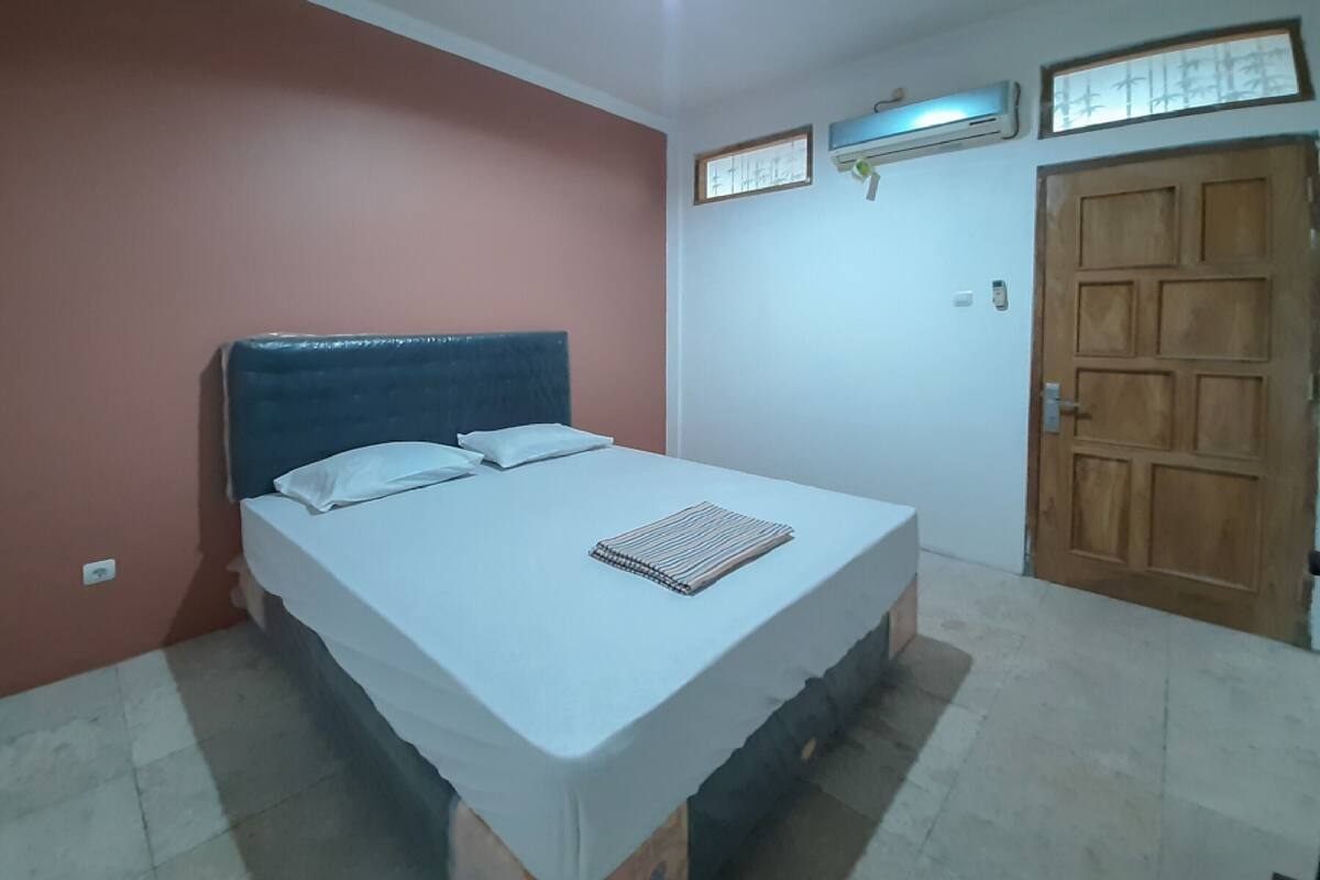 A bedroom with a bed, a wooden door, and a wall-mounted air conditioner.