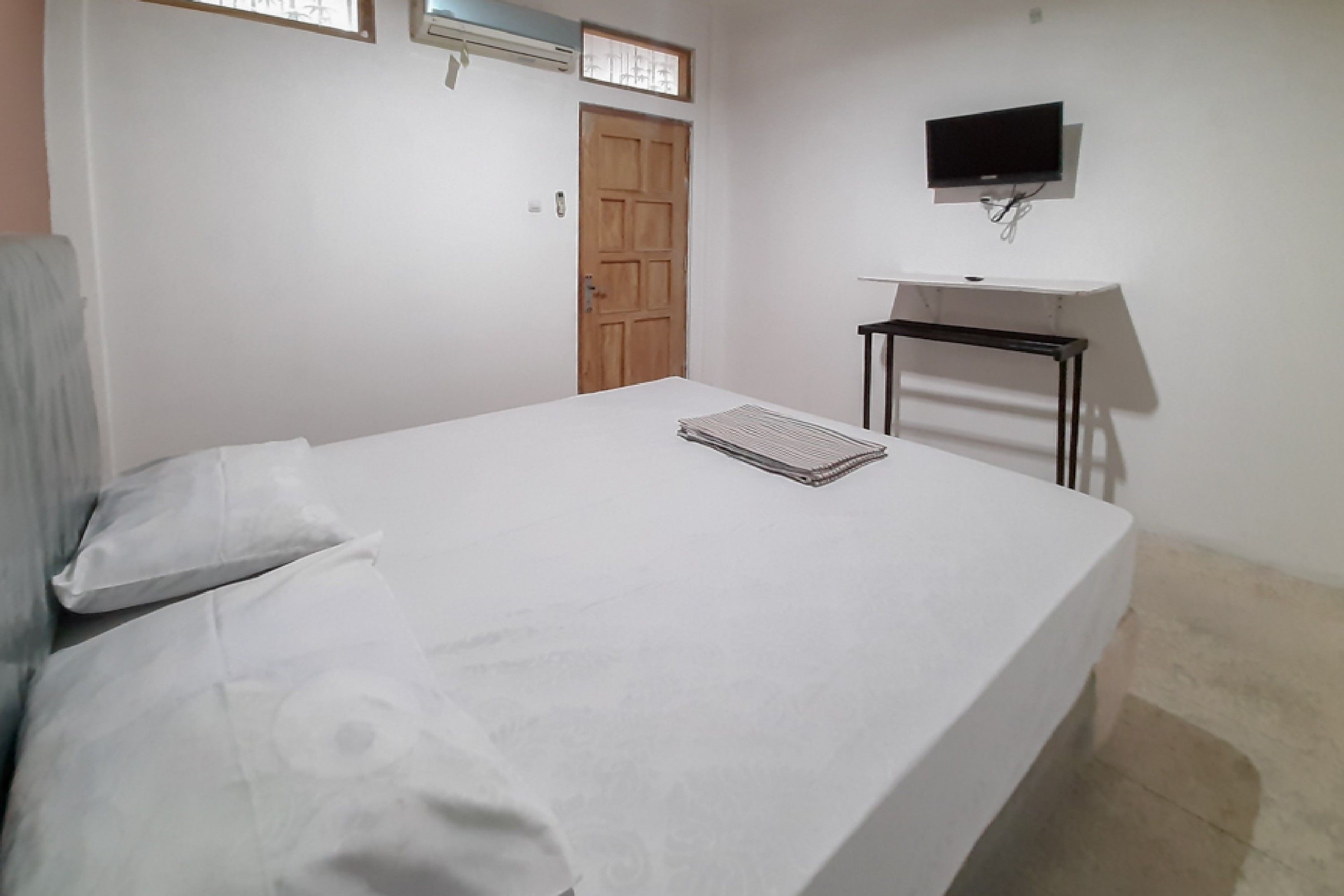A bedroom with a bed, a TV mounted on the wall, and a wooden door.