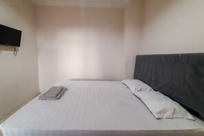 A single bed with a white mattress and a dark headboard. A flat-screen TV is mounted on the wall to the left. - Rejeki Homestay Syariah Malioboro Redpartner (Yogyakarta)