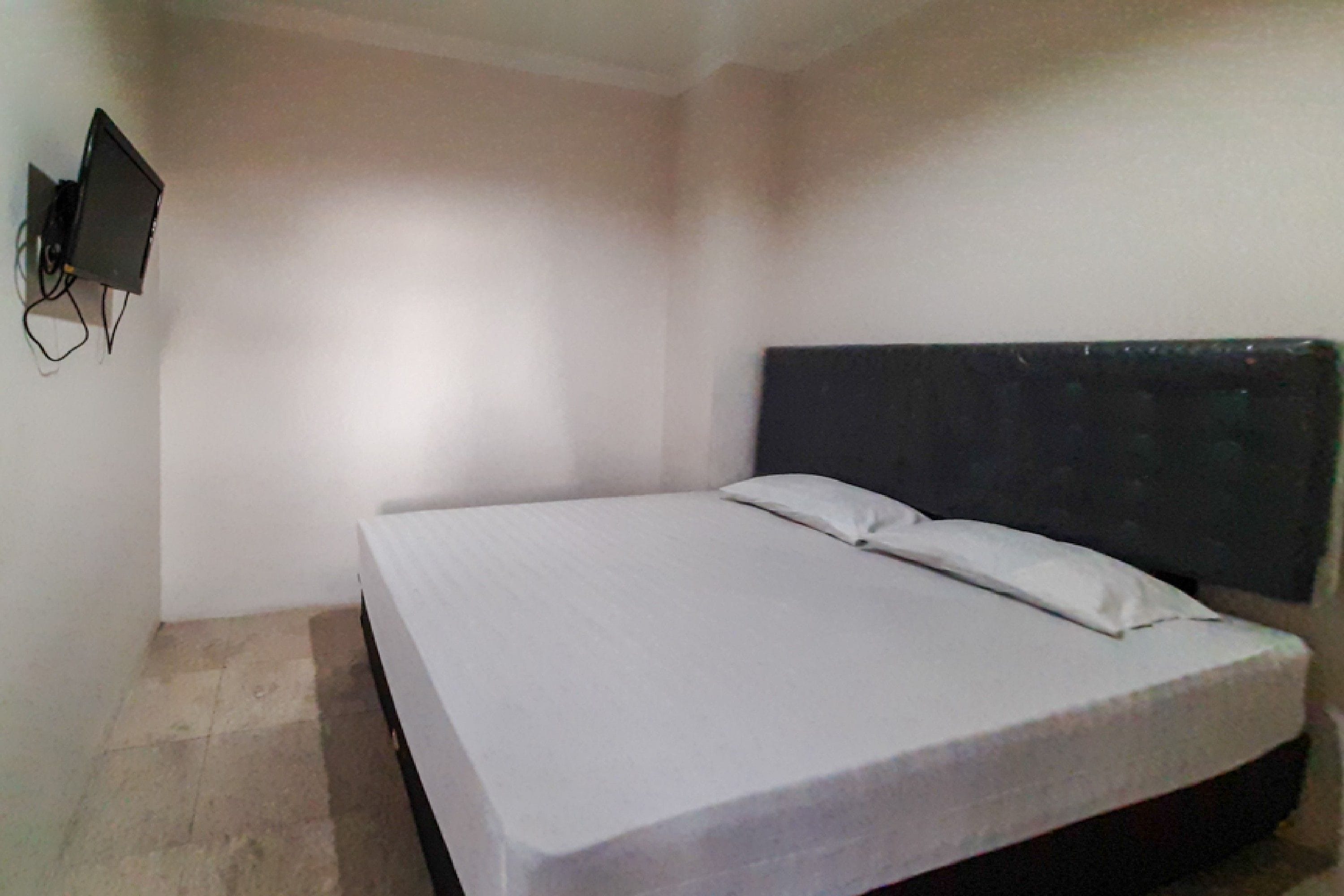Una habitación sencilla con cama, televisor montado en la pared y suelo de baldosas.