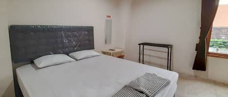 A neatly made bed with a striped blanket, a bedside table, a small table, and a window with curtains.