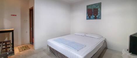 A single-bed room with a wooden headboard, a small table, and a painting on the wall.