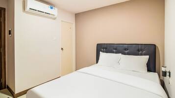 A hotel room with a bed, a door, and an air conditioning unit on the wall.