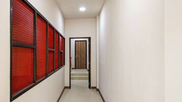 A hallway with a series of windows with red blinds, a wooden door at the end, and a tiled floor.