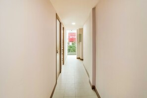 A narrow, well-lit hallway with a tiled floor, leading to a door and a window with a view of greenery outside. - Collection O Kebon Jeruk Near Paskal 23 (Bandung)