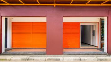A building with two closed orange garage doors, a central red pillar, and a concrete ground level.