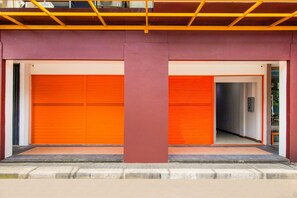 A building with two closed orange garage doors, a central red pillar, and a concrete ground level. - Collection O Kebon Jeruk Near Paskal 23 (Bandung)