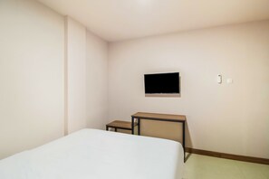 A small, sparsely furnished room with a bed, a desk, and a mounted TV. - Collection O Kebon Jeruk Near Paskal 23 (Bandung)