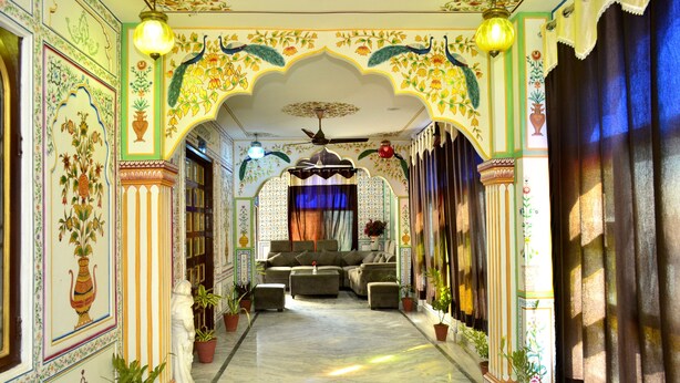 A corridor with ornate walls, a sofa set, and potted plants. - Mahal Rajwada Resort (Jaipur)