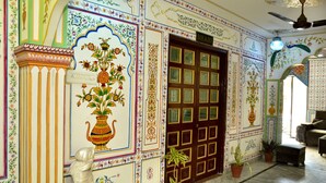 A room with a traditional design, featuring a large door with glass panels, a ceiling fan, and a statue of a woman. - Mahal Rajwada Resort (Jaipur)