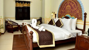 A hotel room with a large bed, a wooden headboard, a bedside table, a chair, and a decorative wall hanging. - Mahal Rajwada Resort (Jaipur)
