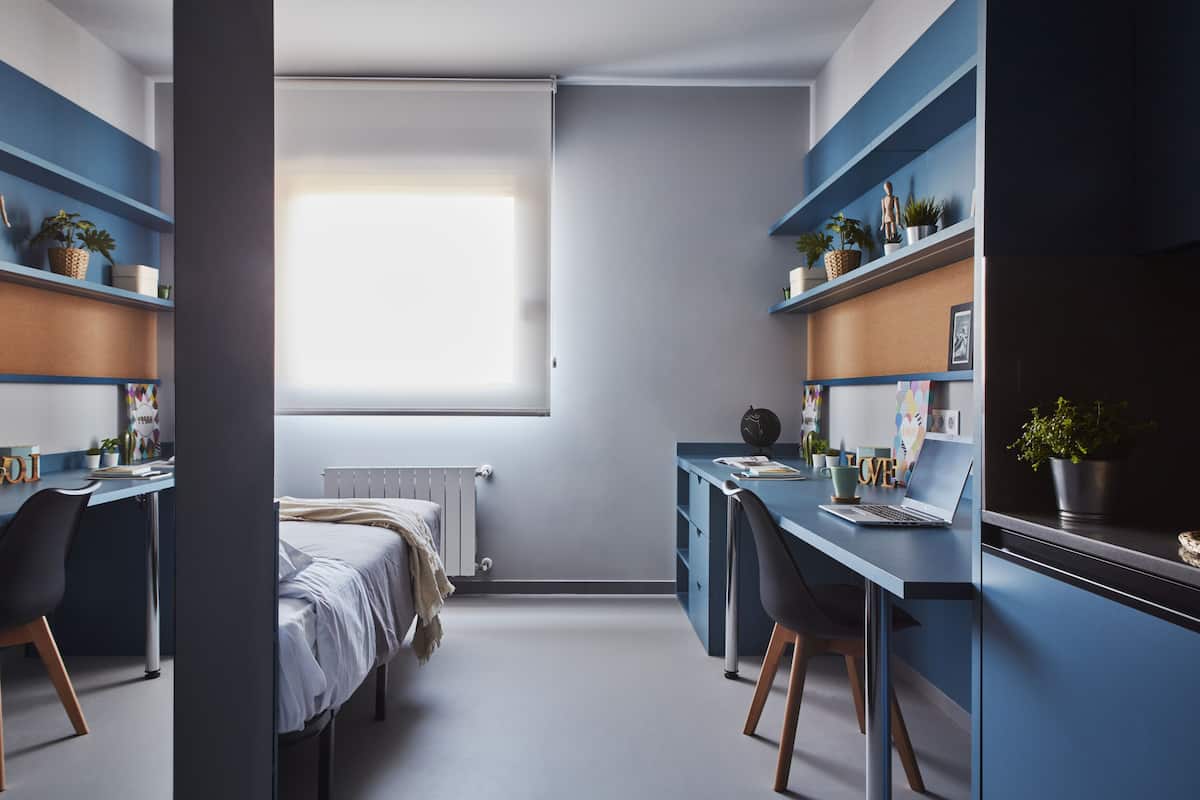 Een moderne kamer met een bed, twee bureaus en kasten.