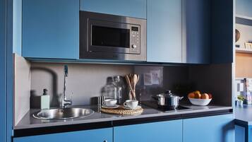A modern kitchen with blue cabinets, a stainless steel microwave, a sink, and a countertop with various kitchen items.