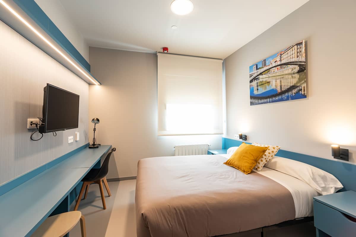 Een moderne hotelkamer met een bed, bureau en stoel, een flatscreen televisie en een schilderij aan de muur.