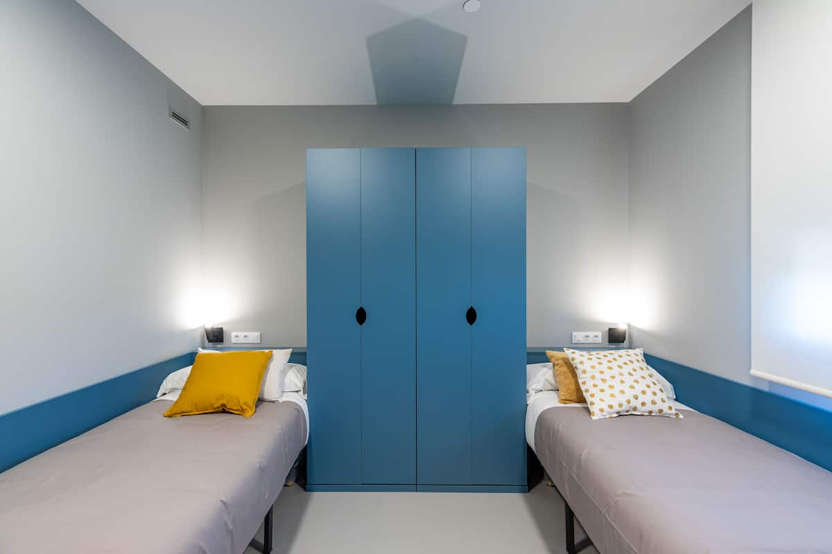 Een kamer met twee eenpersoonsbedden, een blauwe garderobe en nachtkastjes met lampen.