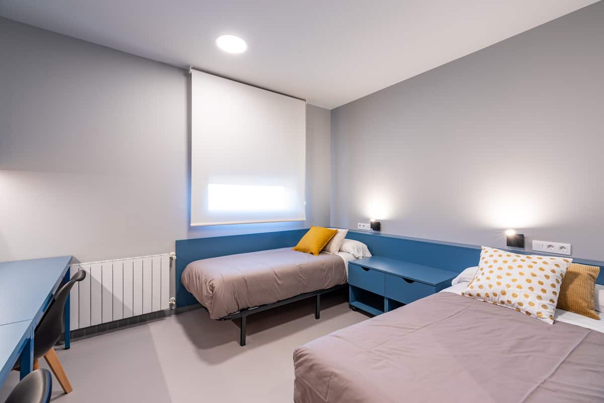 Een slaapkamer met twee bedden, een bureau en een raam.