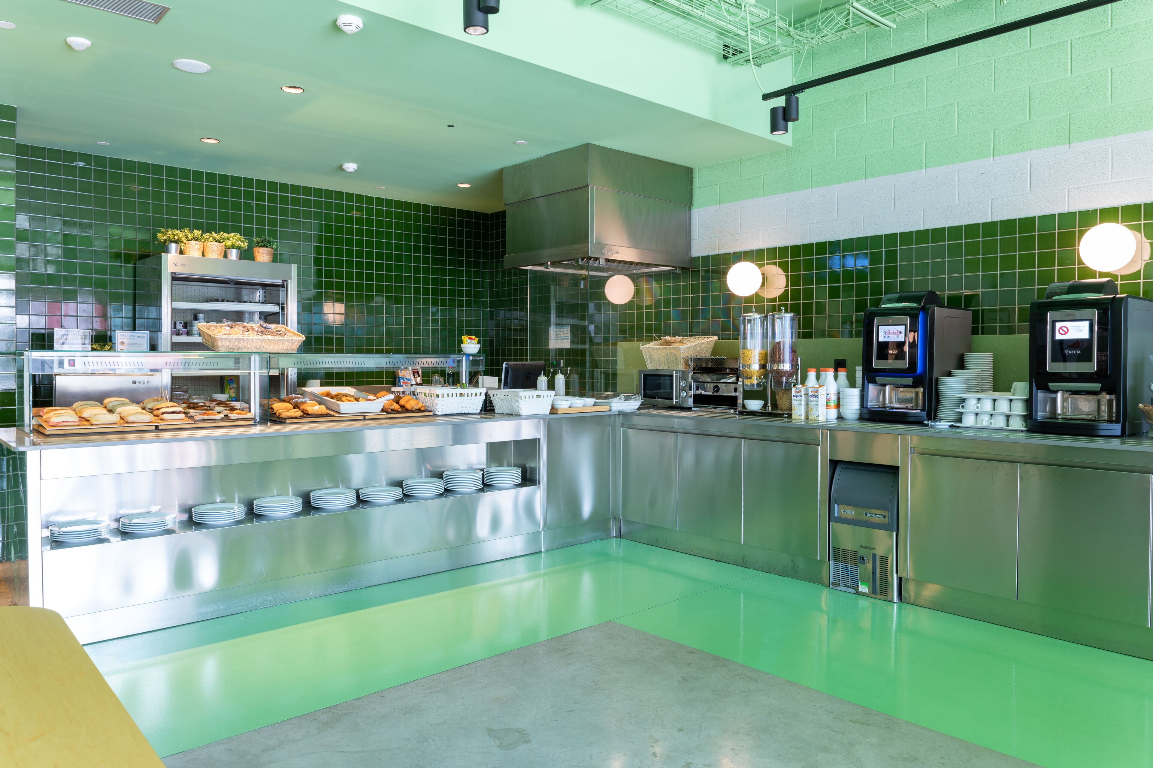 Una cucina moderna con piastrelle verdi, piani di lavoro in acciaio inossidabile e diversi prodotti alimentari esposti.