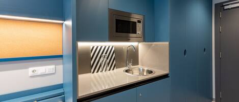 A compact kitchenette with a microwave, sink, and striped towel.