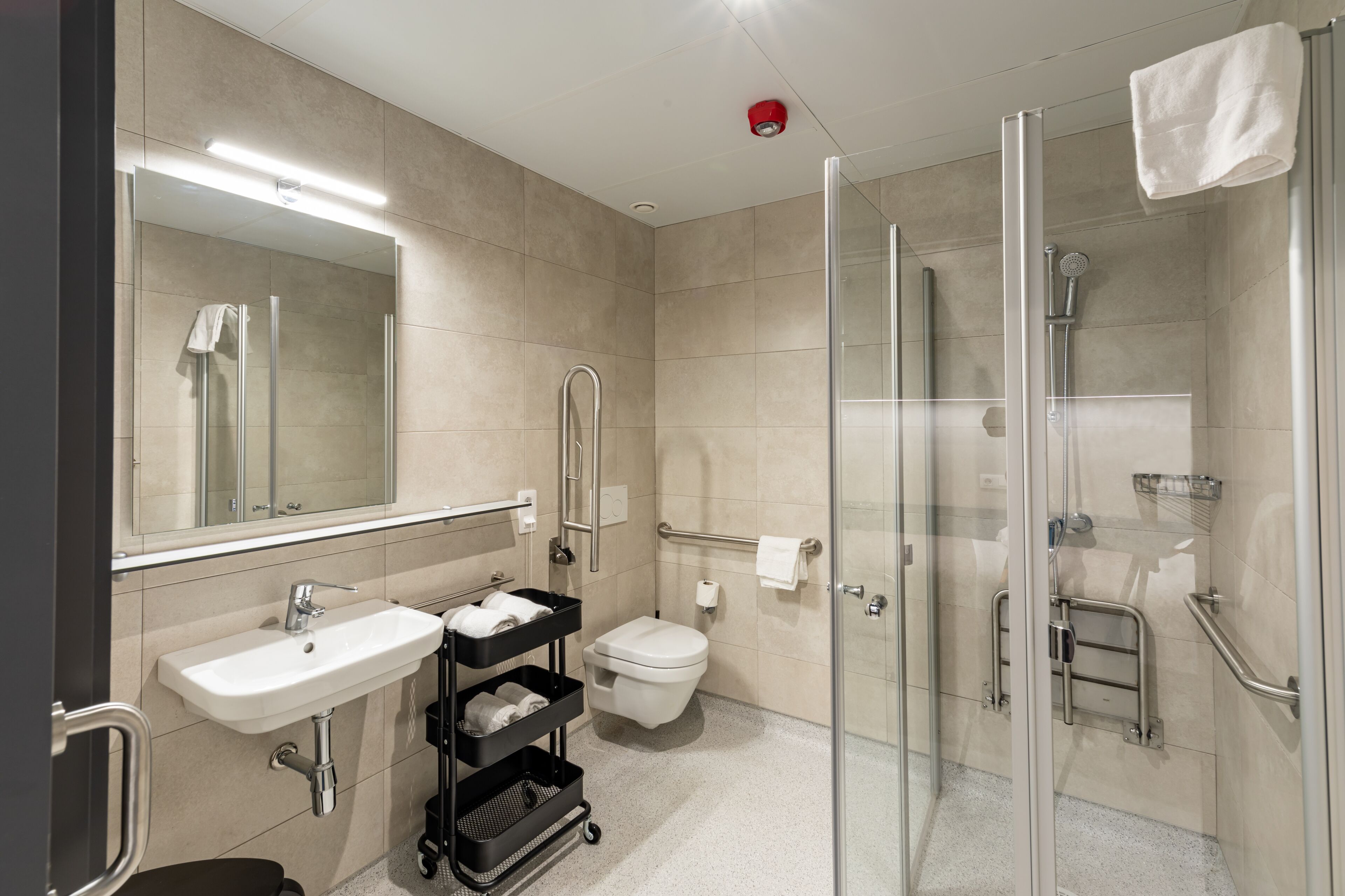 A modern bathroom with a glass shower enclosure, a sink with a towel rack, and a toilet with a grab bar.