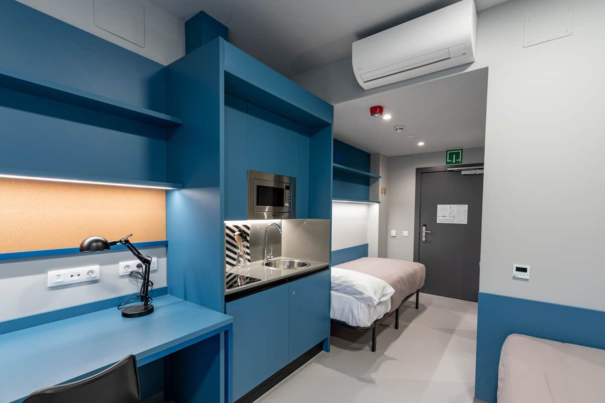 Een compacte hotelkamer met een kitchenette, een bed en een bureau met lamp.
