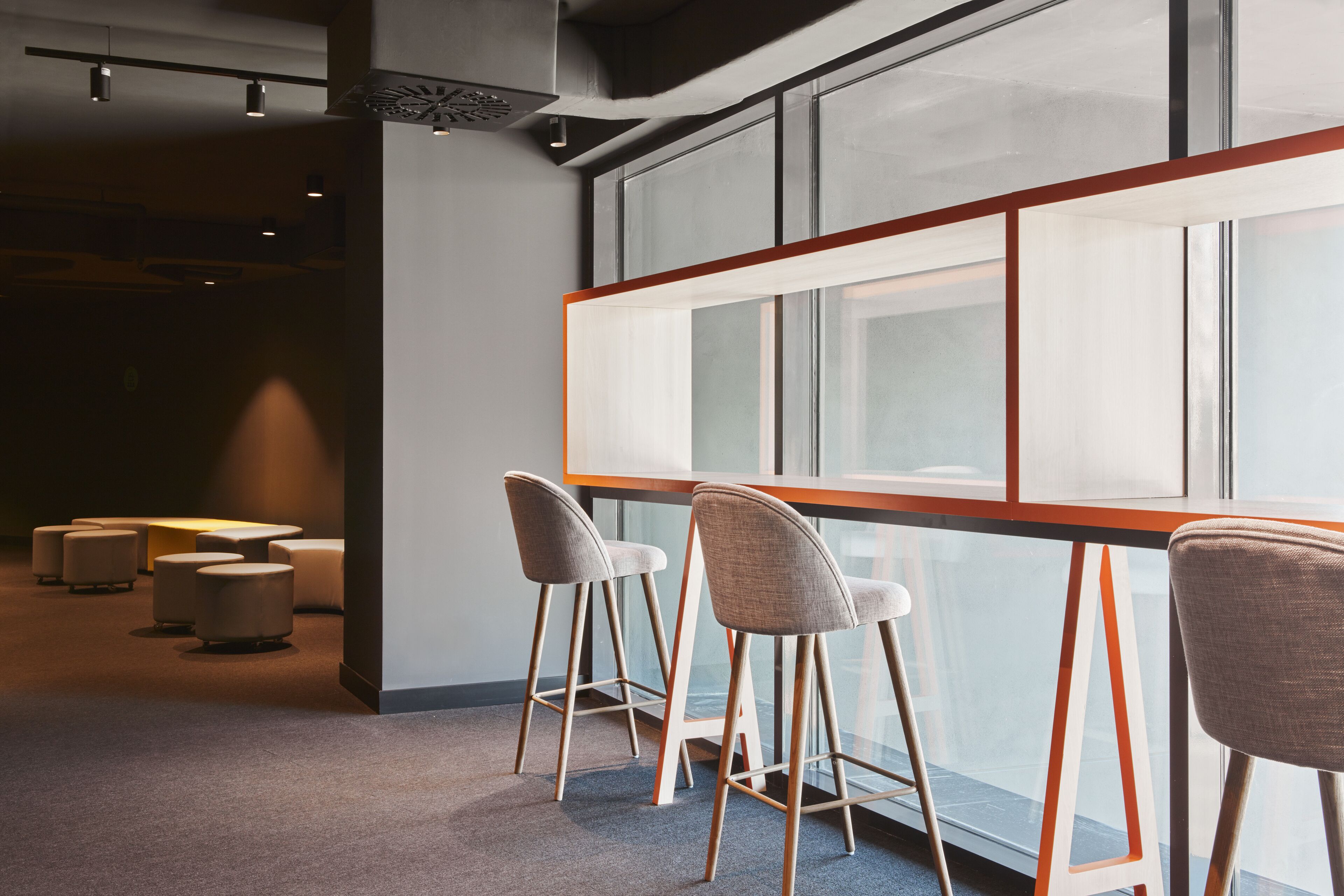 A modern bar area with high stools and a long counter, large windows, and a carpeted floor.