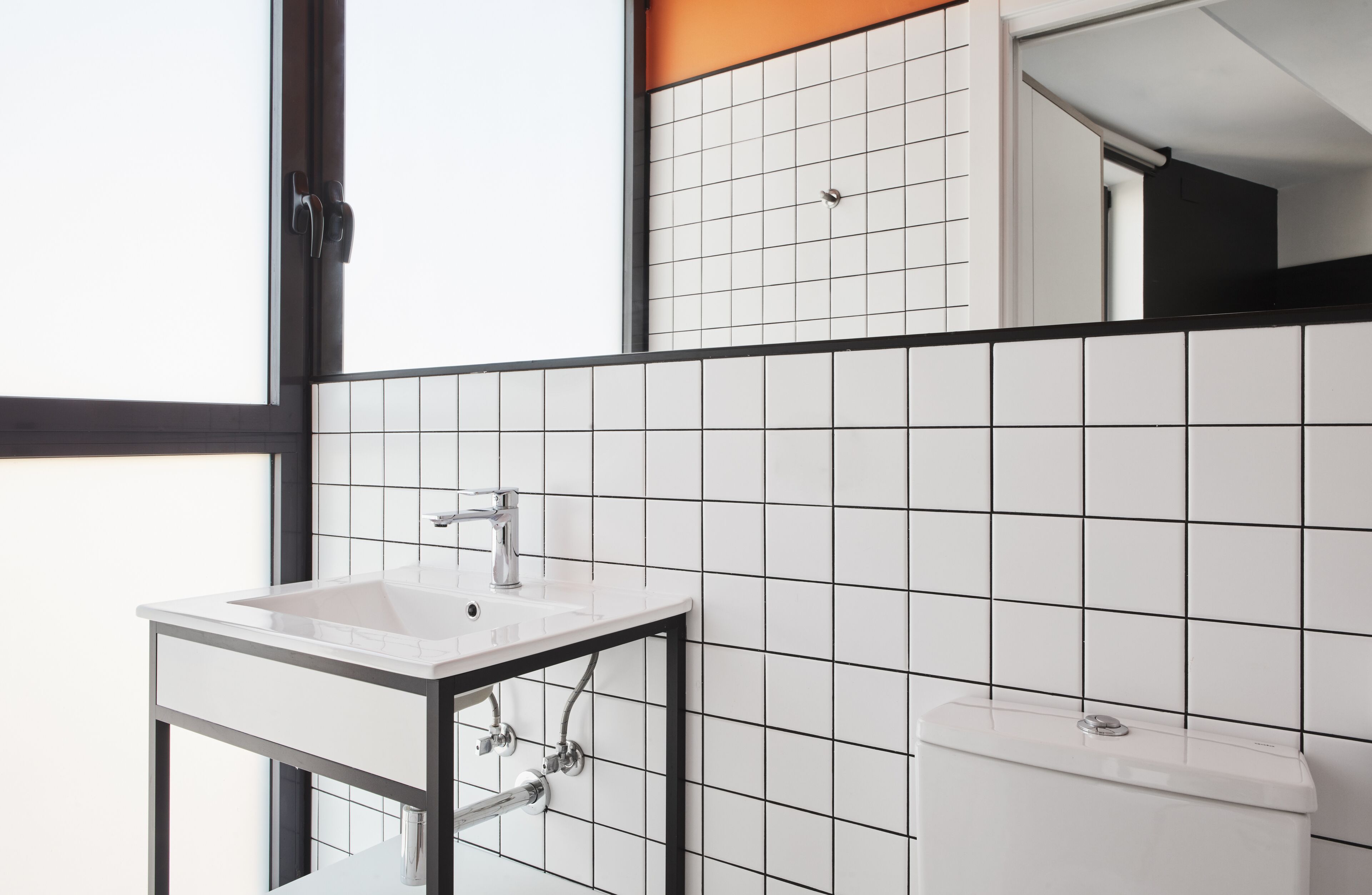 Une salle de bain moderne avec un lavabo blanc, un cadre noir et des murs recouverts de carreaux blancs.