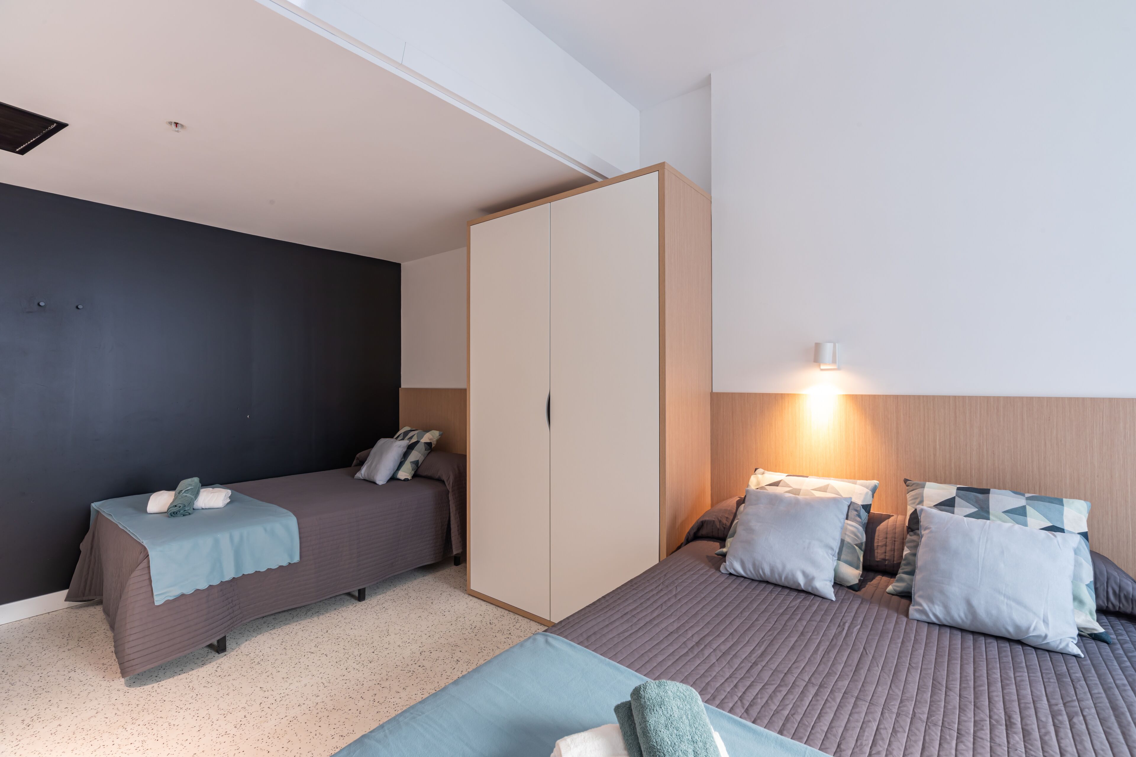 A room with two single beds, a wardrobe, and a bedside table with a lamp.