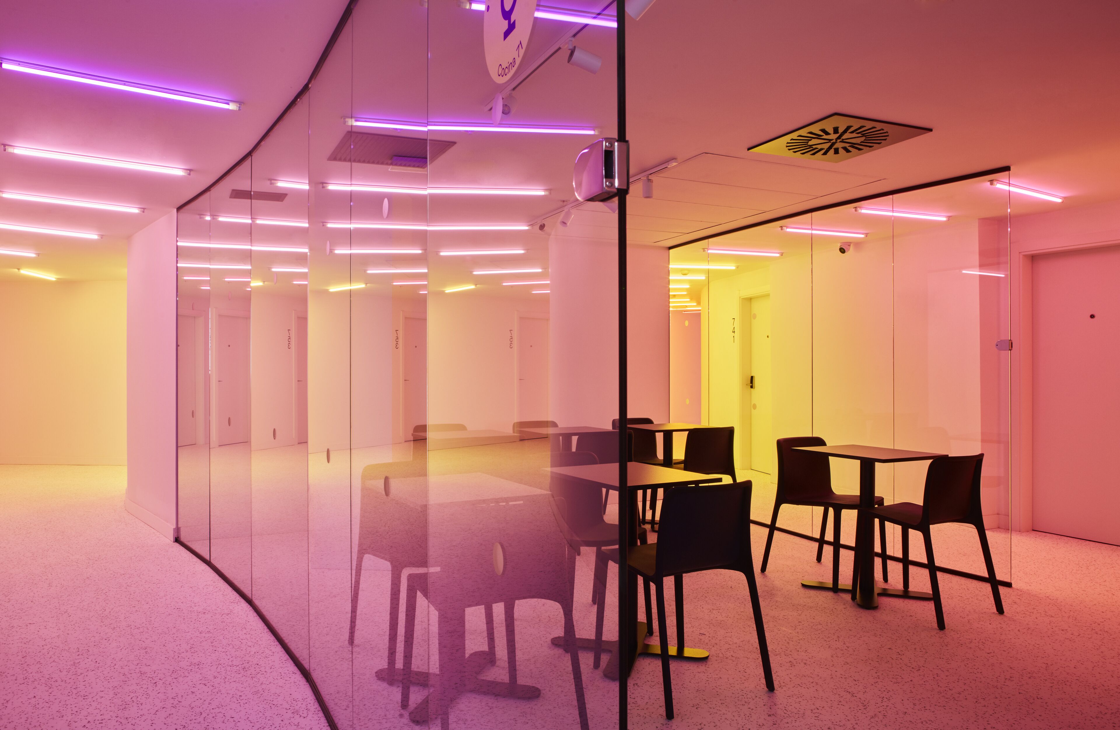Una sala de conferencias moderna con paredes de vidrio, techo blanco e iluminación morada.