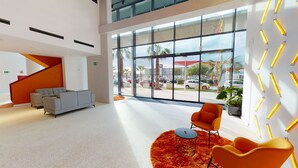 Un vestíbulo moderno con un sofá gris, sillones naranjas y un ventanal con vistas al exterior.