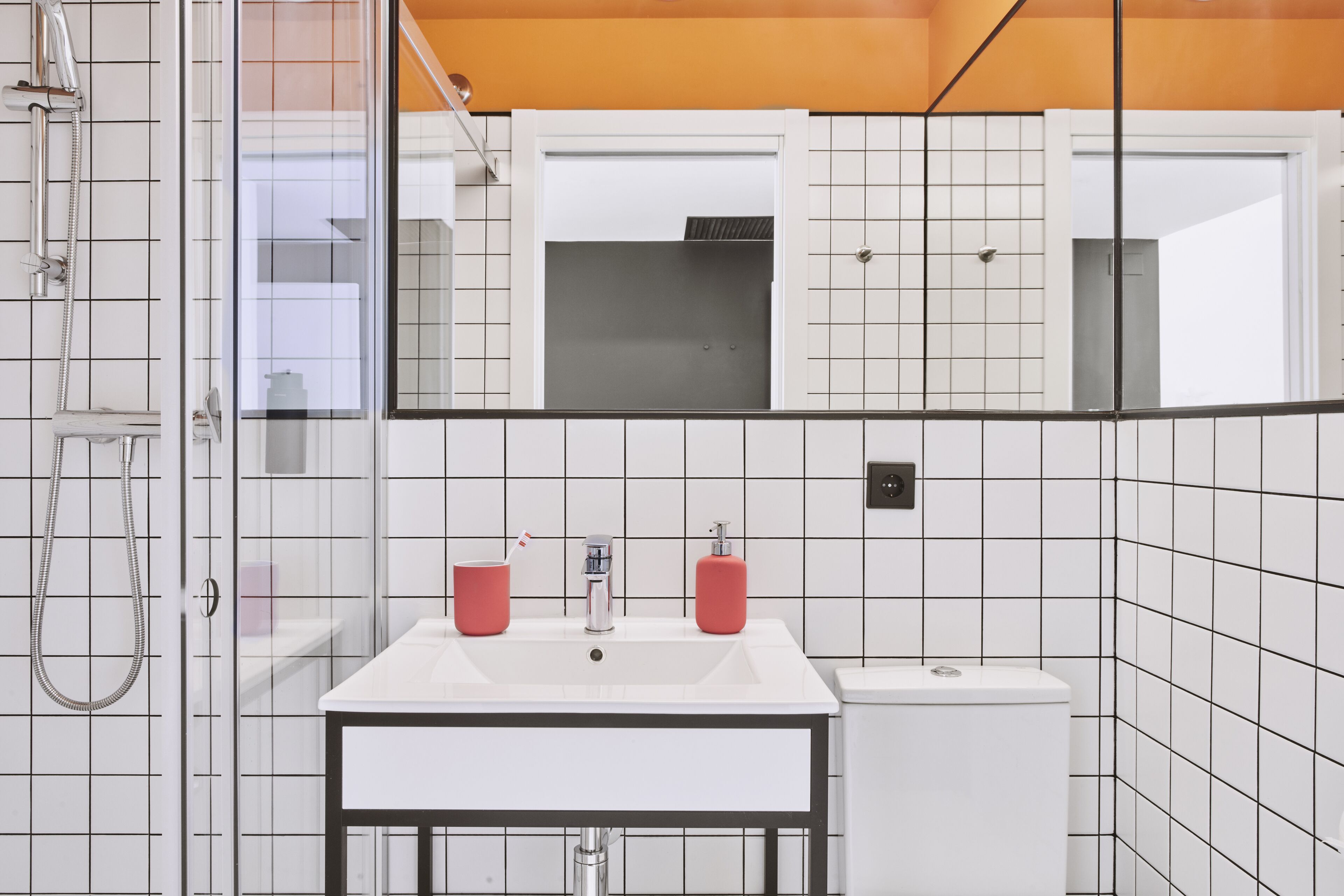 A bathroom with a white sink, two red soap dispensers, a white toilet, and a shower with a handheld showerhead.