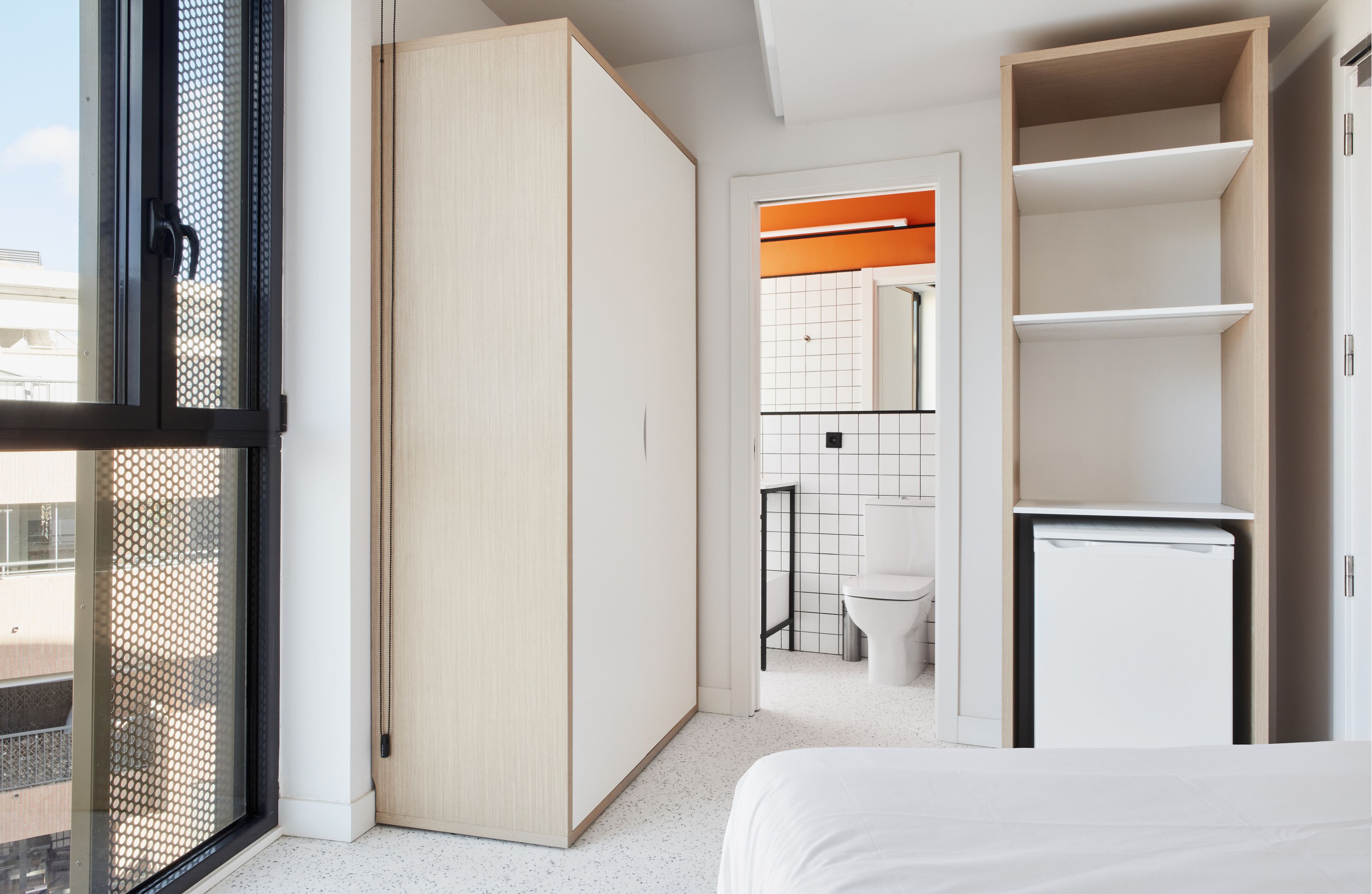 A modern bedroom with a large bed, a wardrobe, and a compact bathroom with a toilet and sink.