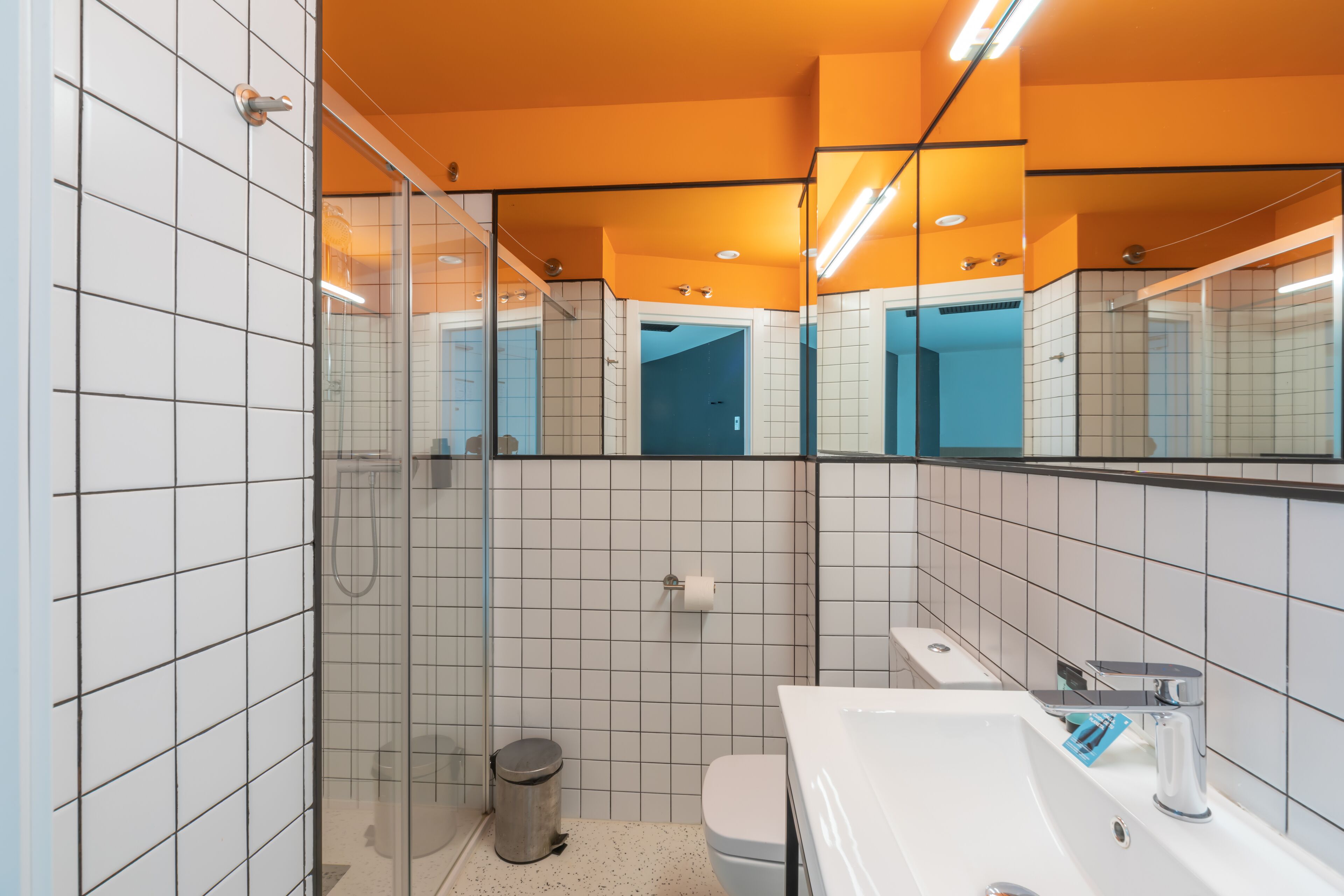 Uma casa de banho moderna com azulejos brancos, cabine de duche em vidro, lavatório branco e espelho.