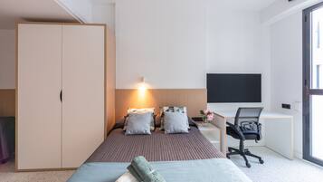 Una habitación de hotel moderna con cama, escritorio, silla, armario y televisor.