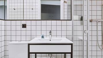 Un baño con lavamanos blanco, espejo y ducha.