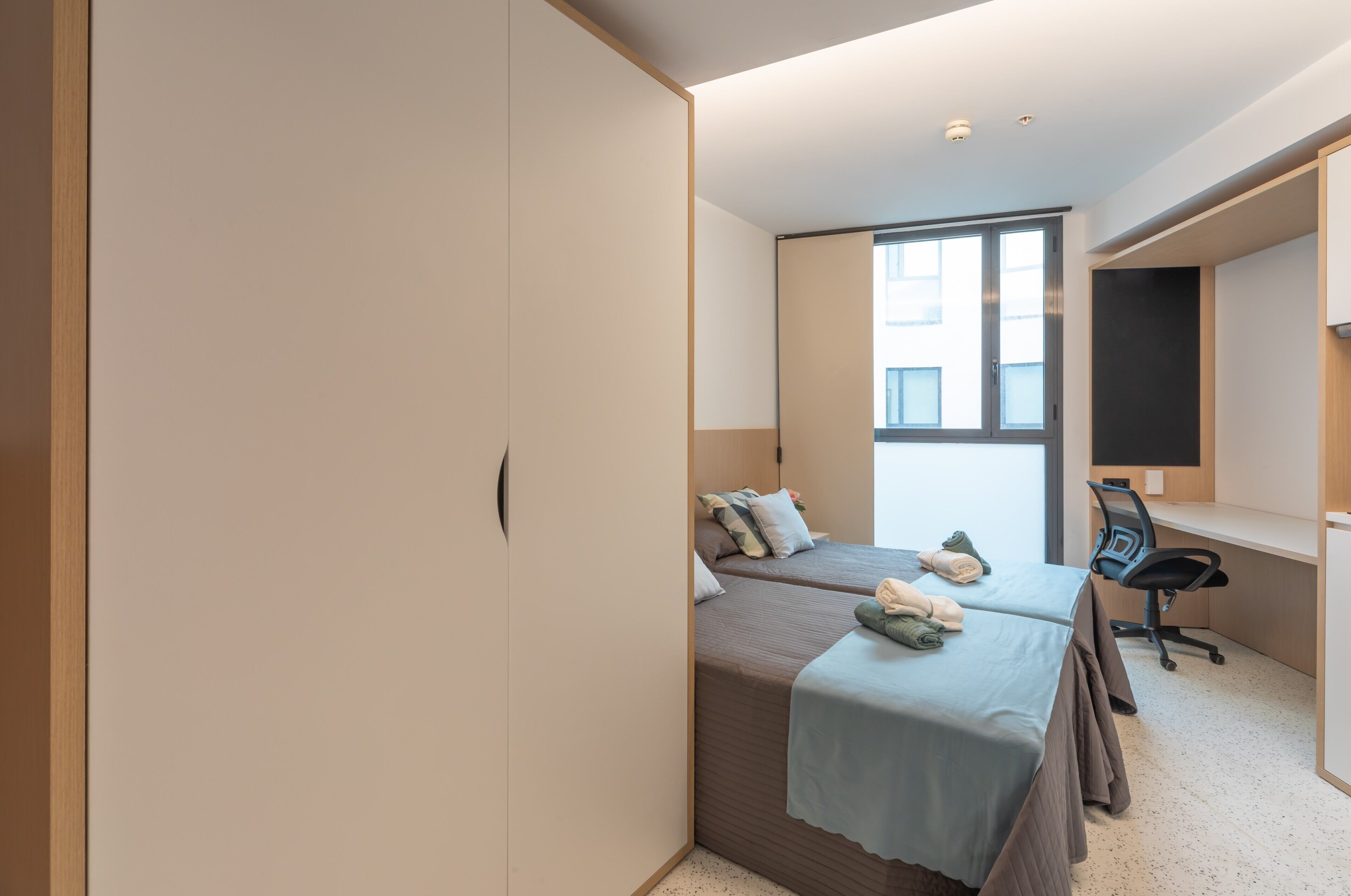 A bedroom with two beds, a desk, and a chair.