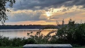 Puiston piknikpöytä, josta avautuu näkymä järvelle ja auringonlaskuun.