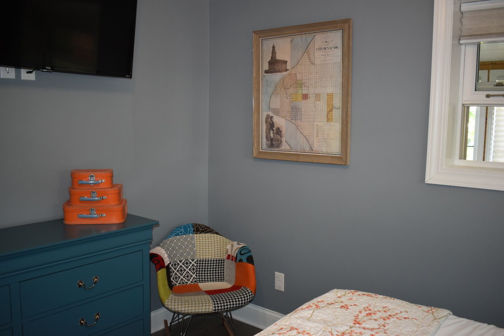 A bedroom with a bed, a dresser, a chair, a map on the wall, and a window.
