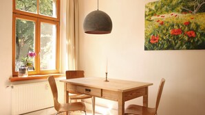 A dining area with a wooden table and chairs, a hanging pendant light, a window with a view of trees, and a painting of a field with red flowers on the wall. - Stylishly furnished apartment in Dresden including bicycles, close to the center (Dresden)