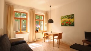A cozy living room with a wooden dining table, two chairs, a sofa, and a TV. - Stylishly furnished apartment in Dresden including bicycles, close to the center (Dresden)