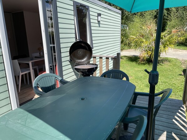 A patio with a table and chairs, a grill, and a covered area with a green umbrella.